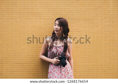 Young female photographer with her camera on yellow background	
