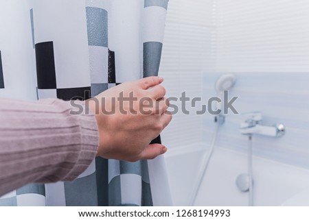 Hand holding shower curtain in white bathroom. Royalty-Free Stock Photo #1268194993