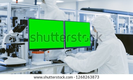 In Laboratory Over the Shoulder View of Scientist in Protective Clothes Working on Personal Computer with Green Screen Chroma Key Template Great for Mock-up. Manufactory Producing Pharmaceutical Items