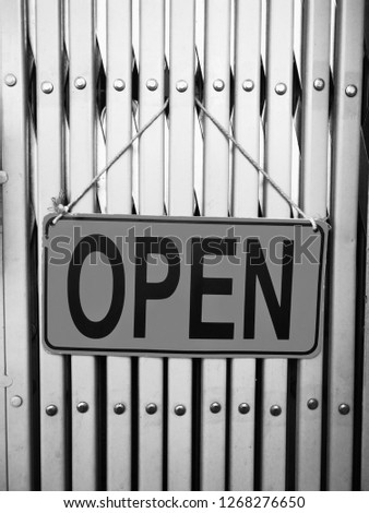 A signal yellow plate "open" hanging in front ot the vintage door in black and white colors.