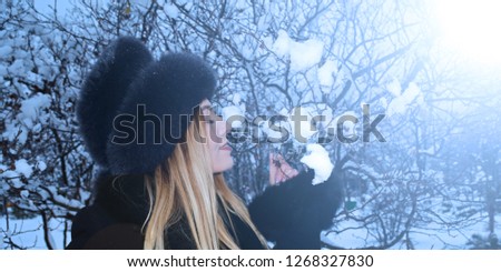 A young girl in a hat sniffs a snow branch in the winter forest
