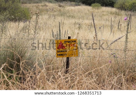 Danger mines! yellow warning sign and barbed wire fence of a minefield in the Israeli Golan Heights by the border with Syria