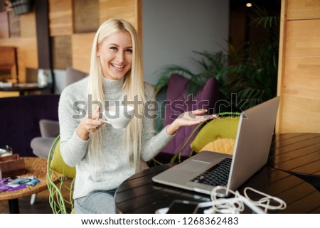 Concentrated at work. Confident young woman in smart casual wear working on laptop while sitting near window in creative office or cafe. Holding a cup of coffee