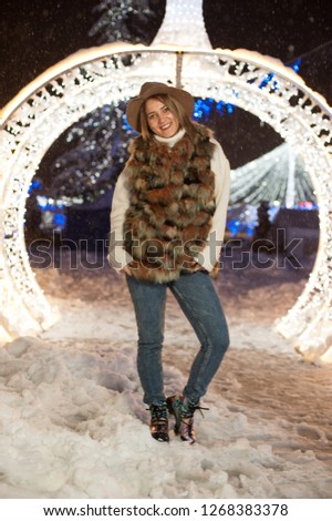 Pretty girl wearing blue jeans and a white top with snowflakes Christmas lights outdoor at night time.