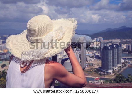 The girl in the hat looks through binoculars on the city bay, toned. Royalty-Free Stock Photo #1268398177