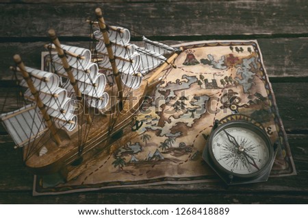 Pirate ship, treasure map and a compass on a wooden table background.