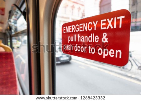 Red emergency exit door sign on the back of the public bus for open in case of emergency. Pull handle and push door to open.