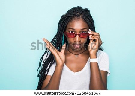 Fashion portrait of young african woman smiling looking on camera in modern sunglasses isolated over blue background
