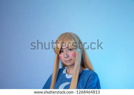 Cute young girl in star cosplay with hearts on cheeks smiles on a blue background