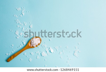 Magnesium Chloride Flakes scattered around brown wooden spoon on blue background. For making foot bath, taking a magnesium-rich bath allows full body exposure to a concentrated solution of magnesium. Royalty-Free Stock Photo #1268469151