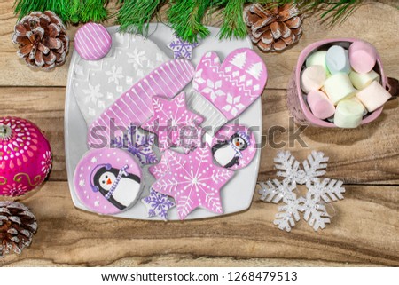 Christmas preparations. Gingerbread, penguins, mittens and hats with asterisks and a mug of marshmallow on a wooden background. Branches of fir and decorations. Festive new year background.