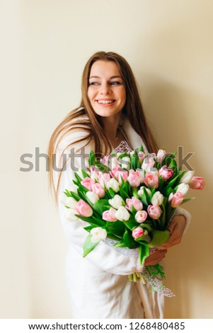 Joyful young woman in a dressing gown holds a bunch of fragrant pink and white flowers and smiles.