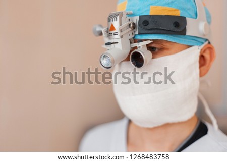 microsurgeon man in a white mask in special medical clothes and glasses with binocular loupes in the operating room. surgeon makes an operation. Hospital equipment