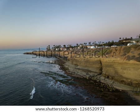 A coastal view of the cliffside of San Diego, California. The light grown cliffs really contrast the ocean blues and wonderful light blue skies that paint the overhead of the photo.