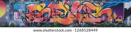 Fragment of graffiti drawings. The old wall decorated with paint stains in the style of street art culture. Colored background texture in warm tones Royalty-Free Stock Photo #1268528449