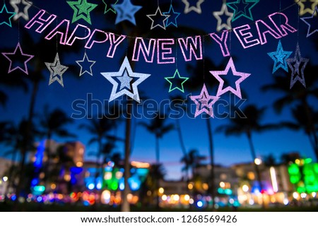 Festive Happy New Year message with stars sparkling above a silhouette view of palm trees and the colorful neon lights of Miami