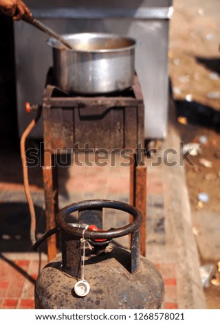  Indian street food vendor cook on gas stove with gas cylinder kept dangerously, in outdoors,road side in busy market                                 