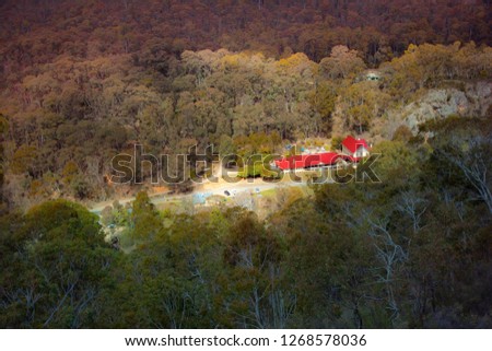 A valley between mountains and hills. The house with bright red roof on the road lit by the sun, surrounding forest in the dark. Yarrangobilly Caves, Kosciuszko National Park, NSW, Australia.