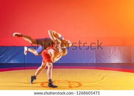 Two greco-roman  wrestlers in red and blue uniform wrestling   on a yellow wrestling carpet in the gym. The concept of fair wrestling