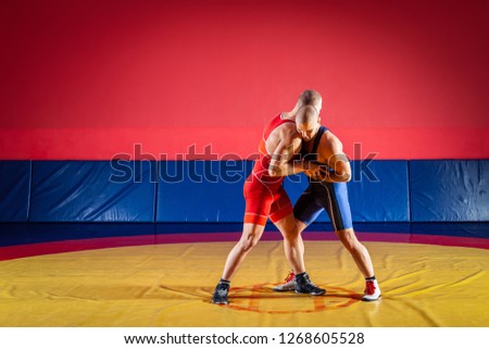 The concept of fair wrestling. Two young men in blue and red wrestling tights are wrestlng and making a hip throw on a yellow wrestling carpet in the gym