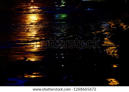 Blurred colorful lights reflection on water surface with river waves and dark background 