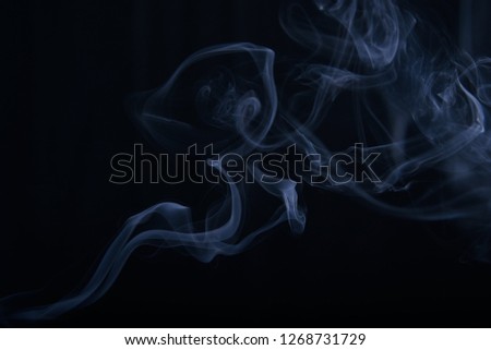 smoke wriggles around in different patterns on a black background. Blue tint.