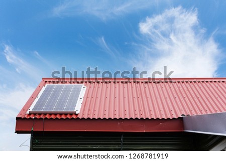 Close up cropped photo of little house with red rivets roof and small solar panel install on top against peaceful blue sky