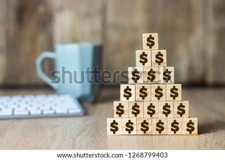 Wooden cubes with a dollar sign lined up with a pyramid on the background of the office desk. Concept of corporation, financial pyramid, leadership, single team, fraud, deception