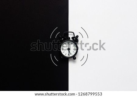 Black ringing alarm clock on black and white background. Concept day and night