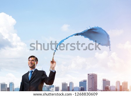 Successful businessman in black suit gesturing and smiling while standing with blue coloured splash against cityscape view on background.