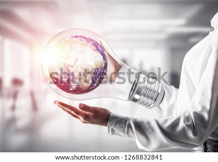 Cropped image of businessman in shirt holding lightbulb with Earth globe inside in his hands. Sunlight on office view background. Elements of this image are furnished by NASA