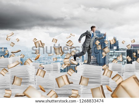 Businessman in suit running with phone in hand among flying books with cityscape on background. Mixed media.