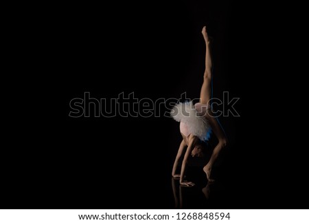 Girl ballerina gymnast in white dress posing on a black background in the studio