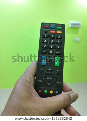 Closeup hand holding remote control of television in the house. 