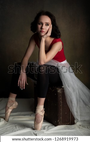 young beautiful dark-haired ballerina girl sad sitting in the Studio on an old suitcase and looking away