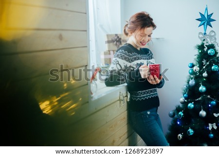girl with a red mug in her hands near the window, on the background of a Christmas tree