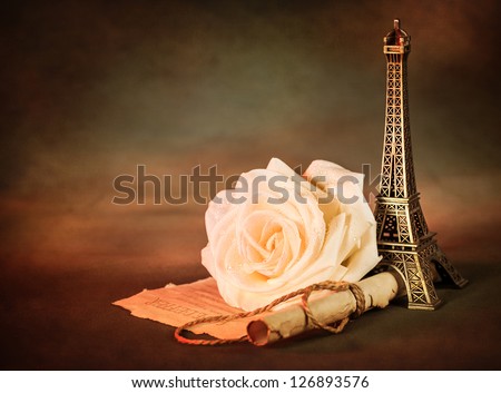 Picture of beautiful still life, old paper scroll with white rose on the table and little Eiffel tower souvenir, dark grunge background, retro style photo, love letter, romantic poem, Valentines day