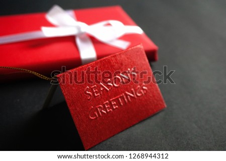 A selective focus shot of a red card with a blurred gift box with a white ribbon over a dark background. The subject used to deliver sense of special occasion