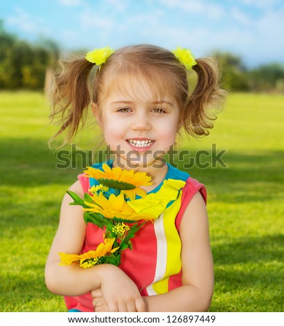 Picture of cute happy little girl wearing colorful dress and holding in hands beautiful sunflower bouquet, adorable small female in garden with fresh yellow flowers, sweet child having fun outdoor