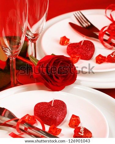 Picture of beautiful romantic table setting, luxury white plates served with silverware and glasses for wine and decorated with red rose flower and heart-shaped candles, Valentine day, love concept