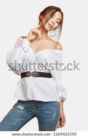Three quarter portrait of girl with brown hair, wearing jeans and a belted blouse. The lady's eyes are closed and she is throwing her head to the side. She is touching her chin on white background.