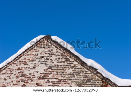 Brick wall and pediment of an old building against blue sky. Some snow on the roof.