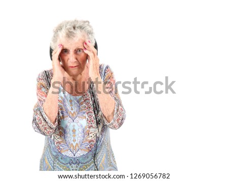 Worried old woman wearing headphones while putting her hands on her head against a white background
