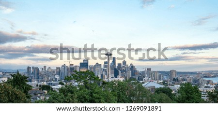 View on the skyline of downtown Seattle during twilight, seen from Kerry Park, with the Space Needle in the middle, Mt Rainier in the back and some orange looking clouds of the sunset above the city.