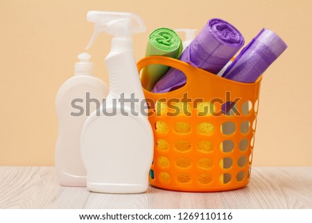 Plastic bottles of dishwashing liquid, glass and tile cleaner, detergent for microwave ovens and stoves, basket, garbage bags, sponges on beige background. Washing and cleaning concept.