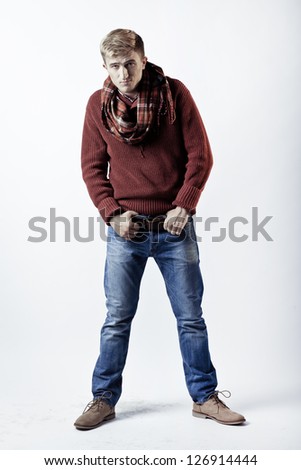 Stylish blond man in sweater, scarf and jeans standing on white background