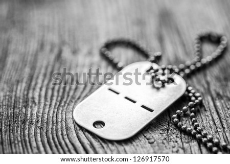 Old blank dog tag on wooden background. Very shallow depth of field with focus on the lower part of a tag