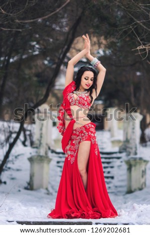 beautiful young girl dancing belly dance in red dress in winter in a park on the snow