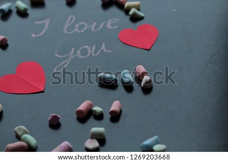 I love you, written chalk on a blackboard. Happy Valentines Day. Valentine's Day theme. Mother's Day. Chalk lettering on blackboard with paper red hearts. Colored chalk lying on a black school board