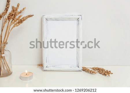 Vertical frame mockup with wild rye bouquet in glass vase near white wall. Empty frame mock up for presentation design. Template framing for modern art. Hygge scandinavian style Natural eco home decor